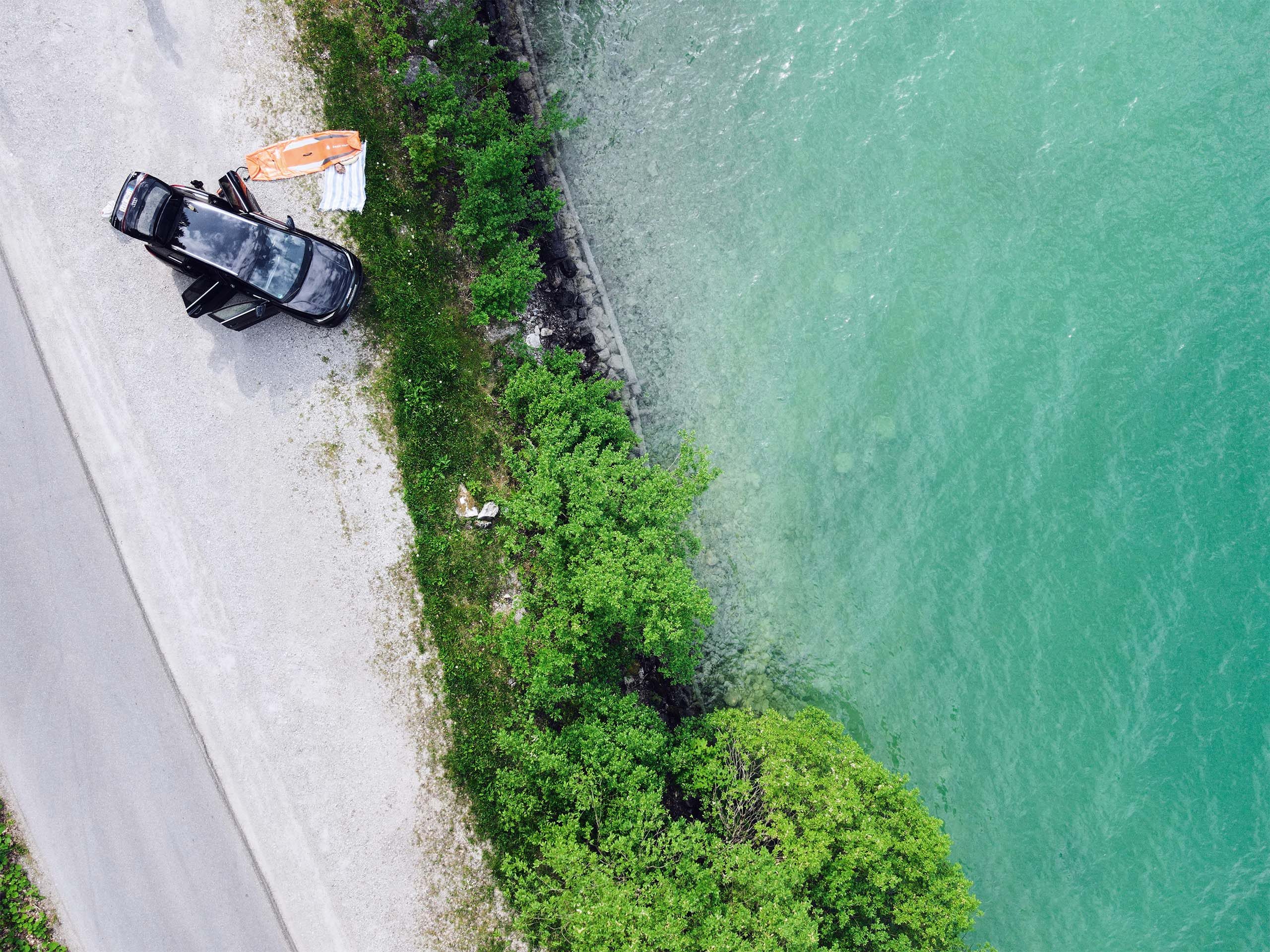 Drohnenaufnahme von einem parkenden E-Auto am See 