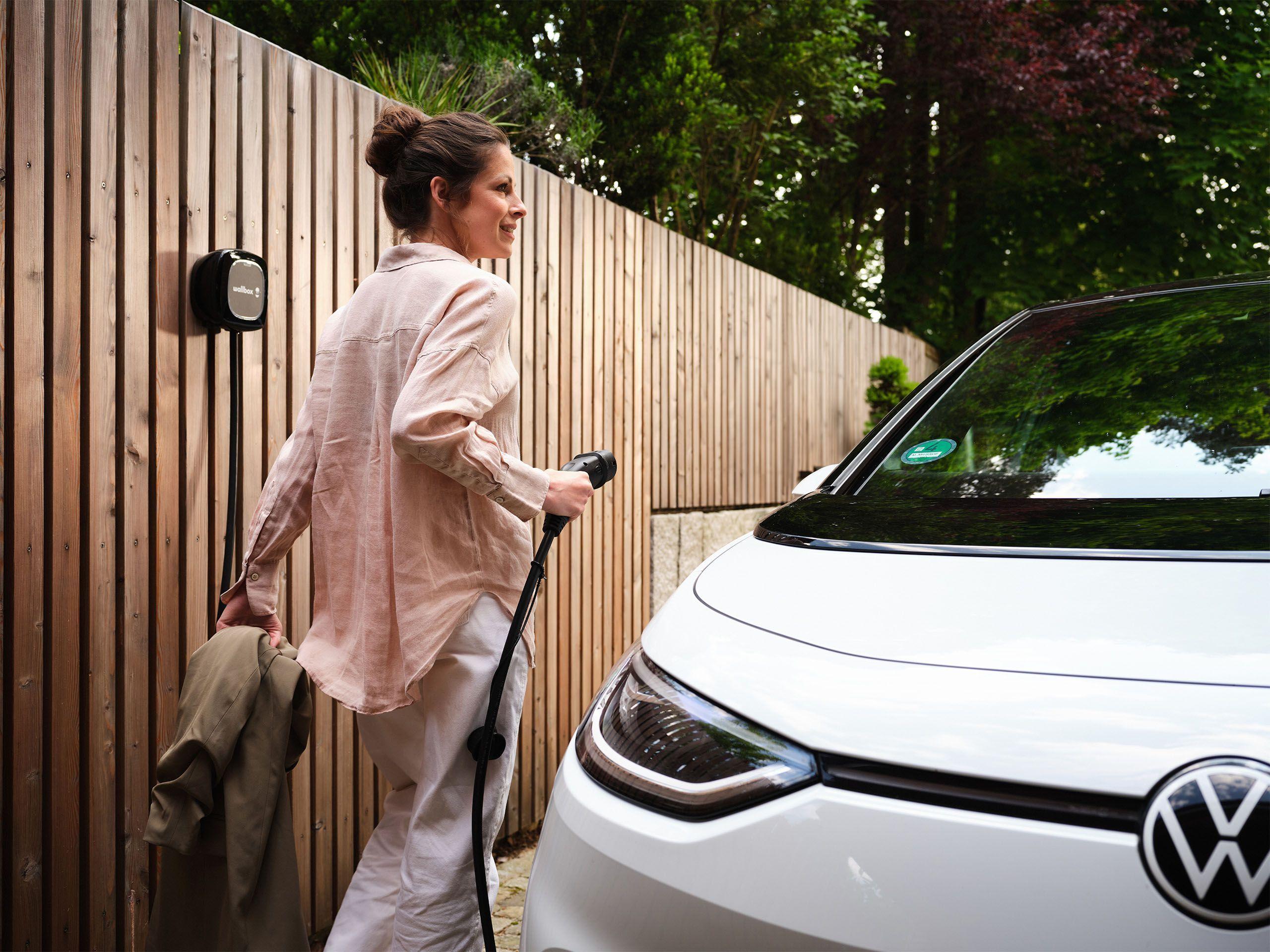 Frau laedt Elektroauto an der Wallbox zuhause