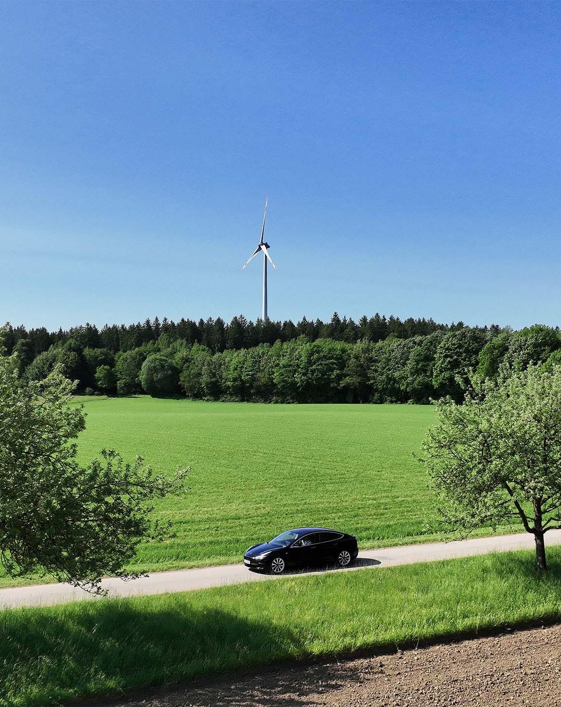 Landschaft mit Elektroauto vor Windraedern
