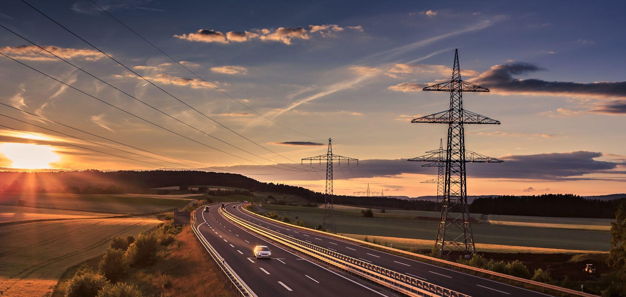 Strommaste im Sonnenuntergang an Autobahn